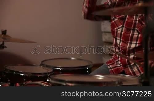 Expressive young hipster drummer throwing up and catching drum stick, hitting the drums while rock band starting to perform music on stage. Handsome teenage musician playing at drum set.