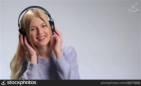 Expressive young woman in headphones singing emotionally along to song on white. Bright positive teenage girl enjoying music, touching earcups with both hands, having fun, positive playful emotions and making funny faces while listening to the music.