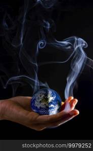 Extended human hand holding a damaged and smoky earth. Smoky earth in our hands