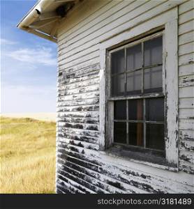 Exterior of weathered abandoned building with peeling paint and window in grassland.