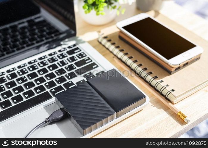 External Hard Disk on Laptop Keyboard with smartphone on notebook,a pencil and flower pot tree on wooden background,Top view office table.