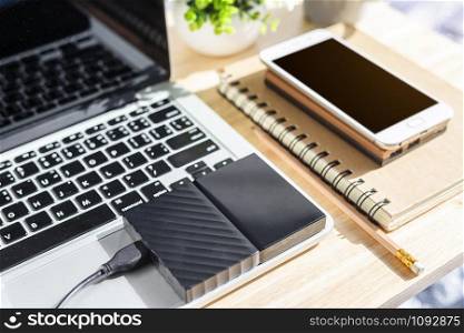 External Hard Disk on Laptop Keyboard with smartphone on notebook,a pencil and flower pot tree on wooden background,Top view office table.