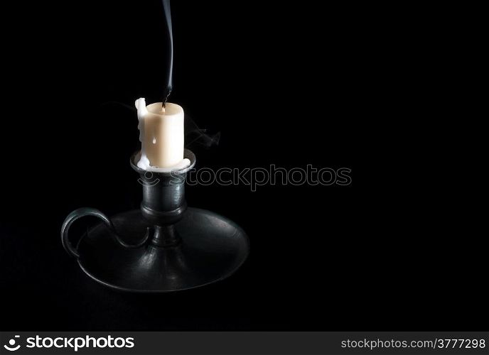 extinguished candle in an old tin candlestick and smoke on a black background