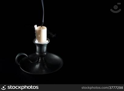 extinguished candle in an old tin candlestick and smoke on a black background