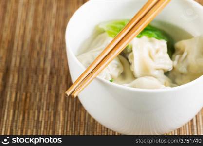 Extreme close up horizontal photo of freshly made wonton with chopsticks on top of white bowl