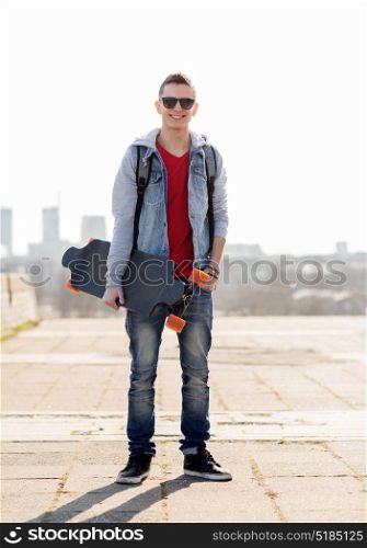 extreme sport and people concept - happy smiling young man or teenage boy with backpack and on longboard in city. happy young man or teenage boy with longboard