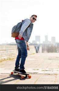 extreme sport and people concept - happy young man or teenage boy with backpack riding on longboard in city. happy young man or teenage boy riding on longboard