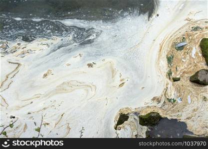 extremely polluted waters, white foam and slick of oil on the sea