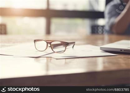 eyeglasses, business document and laptop computer notebook on wooden table, selective focus and vintage tone