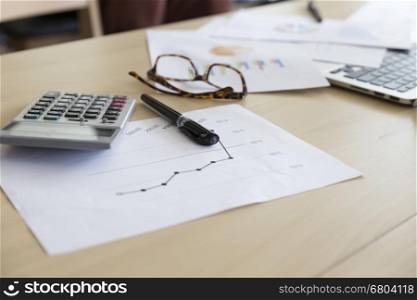 eyeglasses calculator, business document and laptop computer notebook on wooden table