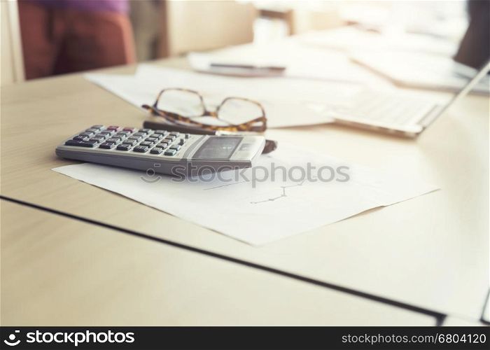 eyeglasses calculator, business document and laptop computer notebook on wooden table, vintage tone