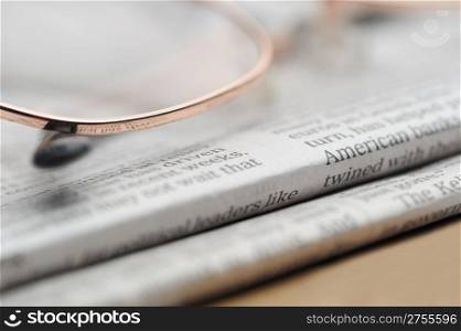 Eyeglasses lie on a pile of newspapers. A photo close up. Selective focus