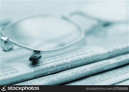 Eyeglasses lie on a pile of newspapers.Blue toned. A photo close up. Selective focus