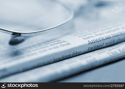 Eyeglasses lie on a pile of newspapers.Blue toned. A photo close up. Selective focus