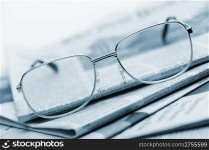 Eyeglasses lie on a pile of newspapers.Blue toned. A photo close up. Selective focus