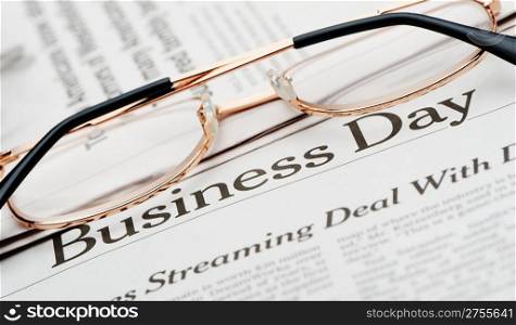 Eyeglasses lie on the newspaper with title Business day. A photo close up. Selective focus