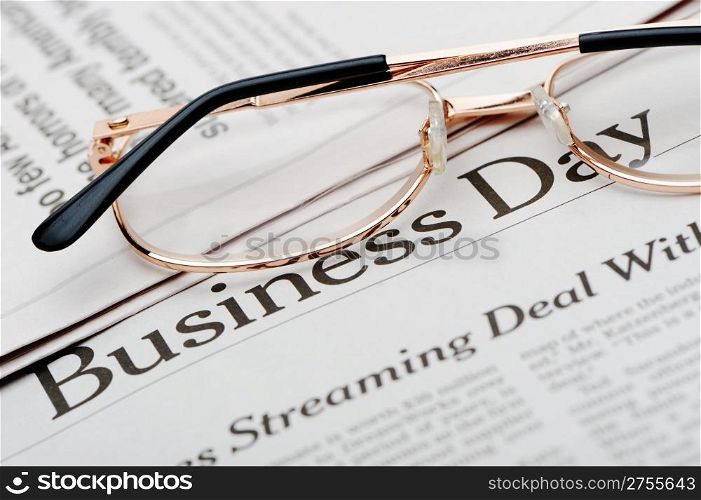 Eyeglasses lie on the newspaper with title Business day. A photo close up. Selective focus