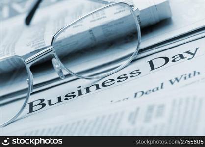 Eyeglasses lie on the newspaper with title Business day.Blue toned. A photo close up. Selective focus