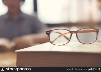 eyeglasses with woman reading book in room, selective focus and vintage tone