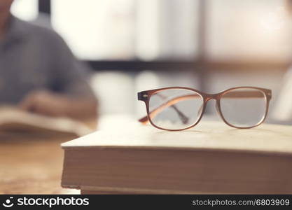 eyeglasses with woman reading book in room, selective focus and vintage tone