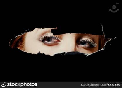 Eyes of a young woman peeping through a hole
