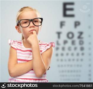 eyesight and vision concept - cute little girl in black glasses over eye test chart background. little girl in glasses over eye test chart