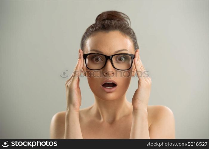 Eyewear glasses woman closeup portrait. Woman wearing glasses holding frame in close-up and looking surprised. Beautiful young caucasian female model on gray background.