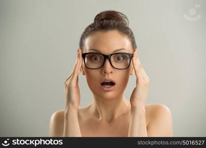 Eyewear glasses woman closeup portrait. Woman wearing glasses holding frame in close-up and looking surprised. Beautiful young caucasian female model on gray background.