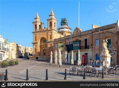 Facade and belfries of the old church of St. Peter on a sunny morning. Marsaxlokk. Malta.. Marsaxlokk. The building of the church of St. Peter on a sunny morning.