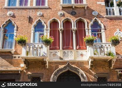 Facade of old building with typical Venetian windows and white balkony with flower pots. Venice, Italy