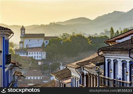Facades of houses and church in colonial architecture in an old street in the city of Ouro Preto with the mountains in the background. Facades of houses and church in colonial architecture in an old street in the city of Ouro Preto