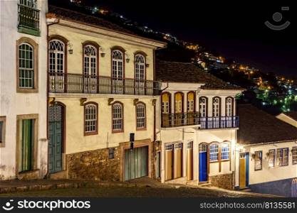 Facades of houses in colonial architecture on an old cobblestone street in the city of Ouro Preto illuminated at night. Facades of houses in colonial architecture on an old cobblestone street illuminated at night
