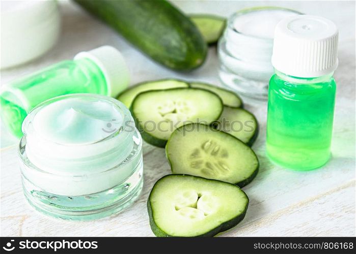 Face cream in a glass jar with cucumber extract next to slices of fresh cucumbers on a white wooden background. Spa treatments.. Face cream in a glass jar with cucumber extract next to slices of fresh cucumbers on a white wooden background.