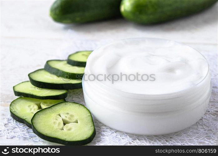 Face cream in a white jar with slices of fresh cucumbers on a white wooden background. Spa treatments.. Face cream in a white jar with slices of fresh cucumbers on a white wooden background.