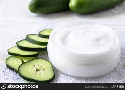 Face cream in a white jar with slices of fresh cucumbers on a white wooden background. Spa treatments.. Face cream in a white jar with slices of fresh cucumbers on a white wooden background.