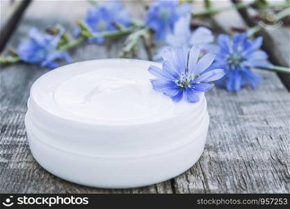 Face cream with the addition of chicory in a white jar near the flowers of chicory on an old wooden table. Health concept. Spa. Face cream with the addition of chicory in a white jar near the flowers of chicory on an old wooden table. Health concept.