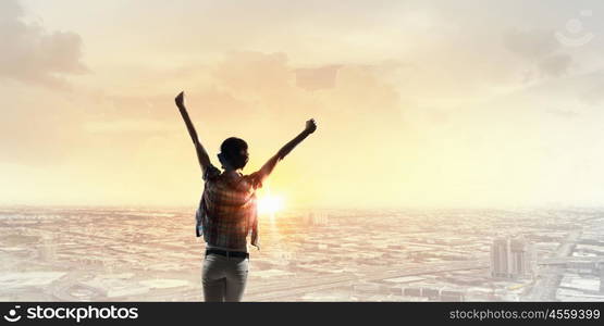 Face new day. Back view of cheerful woman with hands up facing sunrise