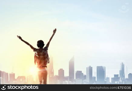 Face new day. Back view of cheerful woman with hands up facing sunrise