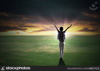 Face new day. Back view of cheerful woman with hands up facing sunrise