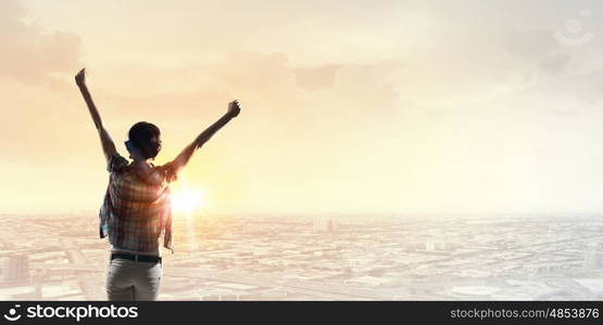 Face new day. Back view of cheerful woman with hands up facing sunrise