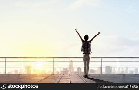 Face new day. Back view of cheerful woman with hands up facing sunrise