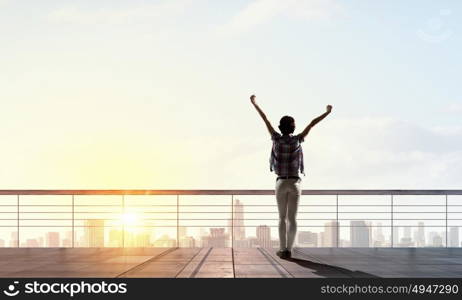 Face new day. Back view of cheerful woman with hands up facing sunrise