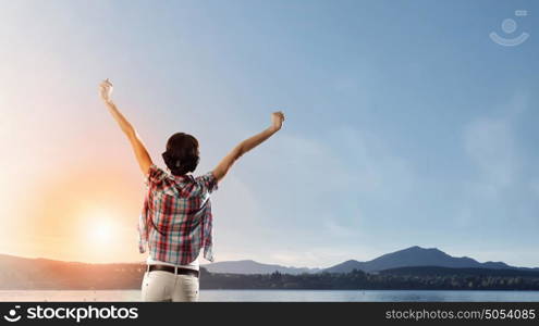 Face new day. Back view of cheerful woman with hands up facing sunrise