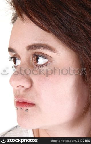 Face of a pretty girl in closeup with three piercing under her lowerlip and with big beautiful eyes, looking away from the camera.