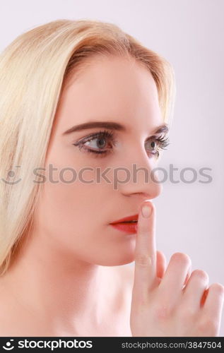 Face of a relaxed blond, young woman with open eyes who lays the forefinger before your red lips.