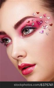 Face of Beautiful Woman with Holiday Makeup Heart. Valentine&rsquo;s Day Make-up. Lips in Pink Lipstick. Makeup detail. Face of Girl on a Pink Background