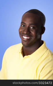 Face of handsome happy African American corporate business man smiling, wearing yellow polo shirt on a blue sky-like background.