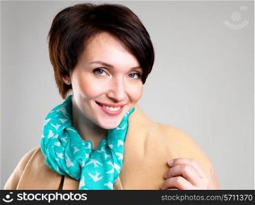 face of happy woman in beige autumn coat with green scarf at studio on the grey background