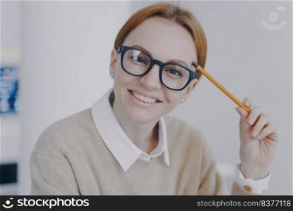 Face of successful attractive girl. Relaxed happy student holding pencil and smiling. Remote study concept. Young european businesswoman or positive manager in glasses.. Face of successful attractive girl. Relaxed happy student holding pencil and smiling. Remote study.