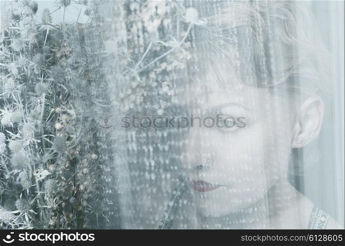 Face of young woman behind transparent cloth with bouquet of dried flowers